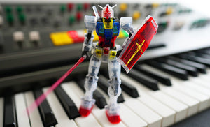 A crystal clear Japanese Gundam with laser sword and shield is standing on a Yamaha CS-80 synthesizer panel. Photo by Christian Halten.